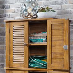 a wooden cabinet with shutters on the doors and shelves in front of a brick wall