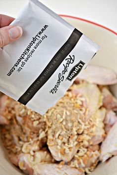 a person holding up a packet of food in front of a bowl full of chicken