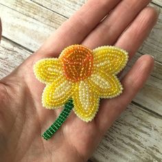 a hand holding a beaded yellow flower on it's palm with green stems