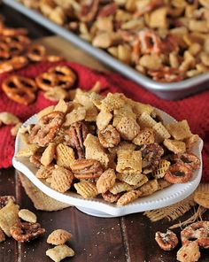 a bowl full of cheesy trail mix next to two trays of pretzels