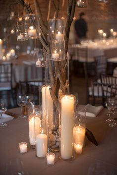 candles are lit on the table in front of an arrangement of branches and glass vases