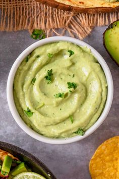 guacamole in a white bowl surrounded by tortilla chips and avocado