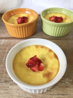 three bowls of soup with strawberries in them on a wooden table top, one bowl is yellow and the other two are green