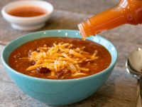 a bowl of chili with cheese being poured into it