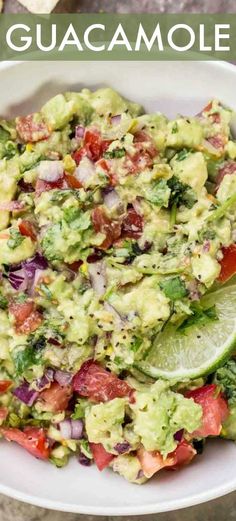 guacamole in a white bowl with lime wedges and tomatoes on the side