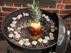 a pineapple sitting on top of a bbq grill with rocks and charcoals