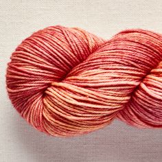 a skein of red yarn sitting on top of a white surface with pink and orange stripes