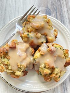 three biscuits covered in gravy on a white plate with a fork next to it