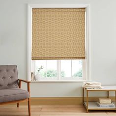 a living room with a chair, table and window covered in roman blind shades on the windowsill