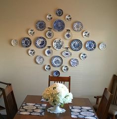 a dining room table with blue and white plates on the wall above it, along with flowers