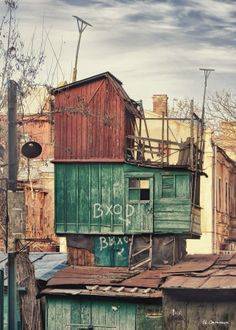 an old wooden building with graffiti on it's side and other buildings in the background