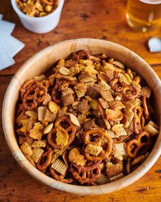 a wooden bowl filled with cheetos next to a glass of beer on a table