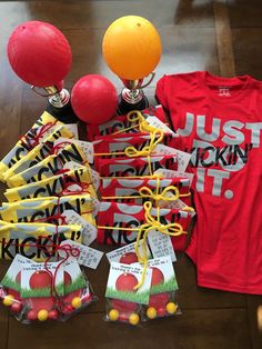 a table topped with lots of red and yellow balloons next to t - shirts that say just kickin'it