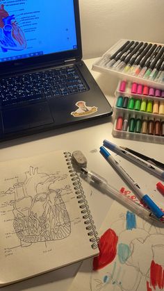 an open laptop computer sitting on top of a desk next to markers and pencils