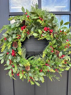 a wreath with berries and greenery is hanging on the front door, next to a window