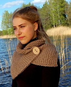 a woman standing next to a body of water wearing a cowl neck sweater with buttons on it