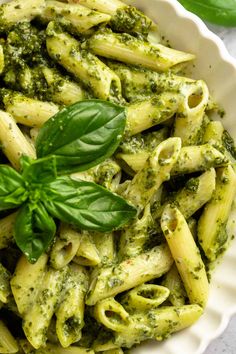 a white bowl filled with pasta and pesto on top of a table next to a green leaf