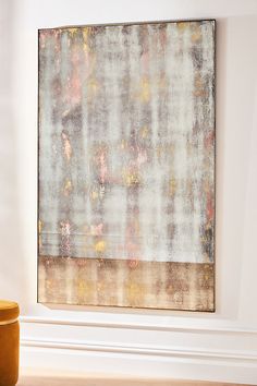 an abstract painting hangs on the wall next to a yellow stool in a white room