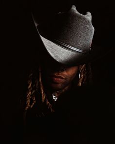 a man with dreadlocks and a cowboy hat on his head in the dark