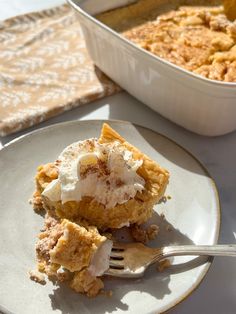 a piece of pie on a plate with a fork next to it and a casserole dish in the background