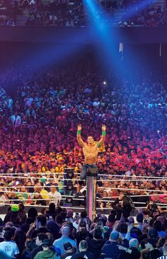 a man standing on top of a wrestling ring holding his hands up in the air