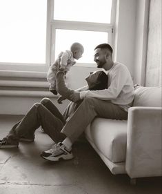 a man sitting on top of a white couch next to a baby in his lap