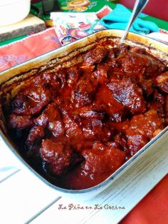 a casserole dish with meat and sauce in it on a red table cloth