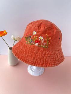 an orange hat with flowers on it next to a white vase