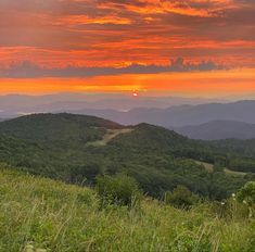 the sun is setting in the distance over some hills and valleys with trees on each side