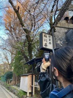 a woman is taking a photo with her cell phone in front of a street sign