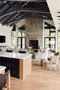 a large open concept living room and kitchen area with wood flooring, stone fireplace, exposed beams, white couches and chairs