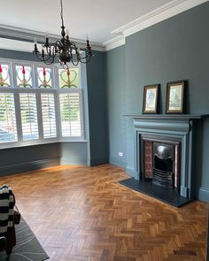 an empty living room with wood floors and blue walls, two framed pictures on the fireplace