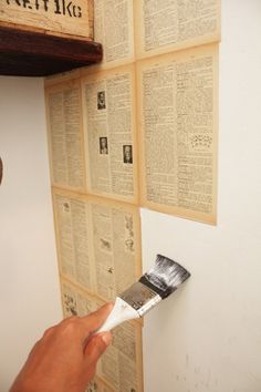 a person holding a paintbrush in front of a wall with old books on it