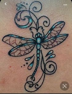 a dragonfly tattoo on the back of a woman's shoulder, with swirls and