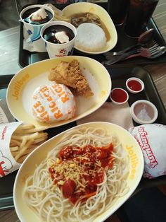 two plates with noodles, chicken and ketchup sit on a tray next to sodas