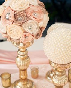 a gold vase filled with pink flowers on top of a white table covered in candles