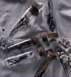 four glass bottles with dried flowers and branches in them sitting on a silver cloth covered surface