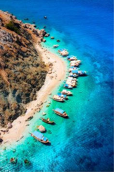 an aerial view of several boats docked at the shore on a clear blue water day