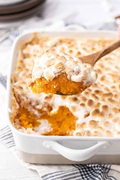 a spoon with some food in it on top of a white dish filled with bread