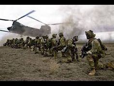 a group of soldiers walking in front of a helicopter