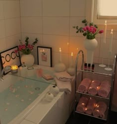 a bath tub with candles and flowers in the corner, next to a shelf filled with towels