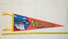 a red and yellow pennant with niagara falls on it next to a measuring tape that says niagara falls canada