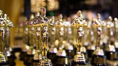 many oscar statues are lined up on the table in front of each other and one is holding an award