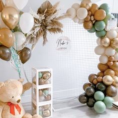 a teddy bear sitting in front of a balloon arch