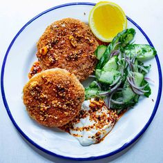 two crab cakes on a plate with salad and lemon wedges