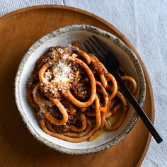 a bowl filled with pasta and sauce on top of a wooden table next to a fork