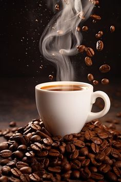 a cup of coffee with steam rising out of it on top of some coffee beans