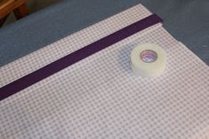 a roll of toilet paper sitting on top of a blue bed sheet covered in purple ribbon