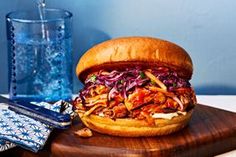 a pulled pork sandwich with coleslaw on a cutting board next to a glass of water