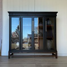 a large black cabinet with glass doors on the top and bottom, in front of a white wall